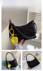 Detail of black quilted puffer bag featuring a yellow sunflower charm and leather strap