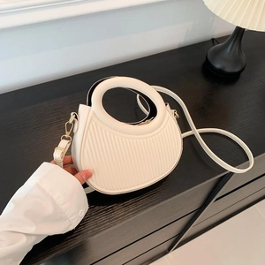 Fashionable beige pleated crossbody bag with a circular handle on a dark wood table