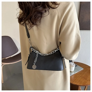 Detail of black crescent shoulder bag with silver chain worn over a beige trench coat