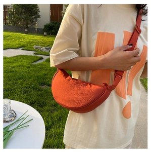 Burnt orange nylon crescent crossbody bag with adjustable strap shown in outdoor setting