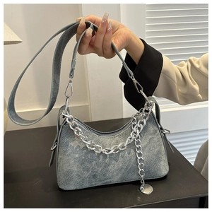 Detail of crescent denim crossbody bag featuring a thick silver chain and metal charm