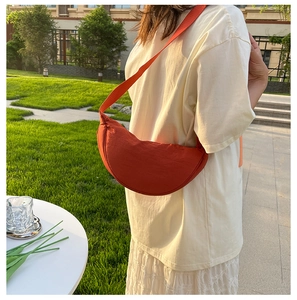 Vibrant orange nylon crescent cross-body bag shown worn by a model in a sunny outdoor park