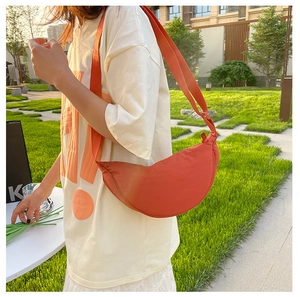 Outdoor shot showing an orange-red crescent nylon shoulder bag on a model side-view
