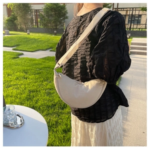 Outdoor shot of an off-white crescent crossbody bag with adjustable wide strap on grass