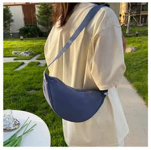 Outdoor shot of a blue nylon crescent shoulder bag shown on model in a casual park setting