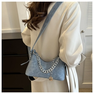 Blue denim texture crescent shoulder bag with chain strap shown on model in a home setting