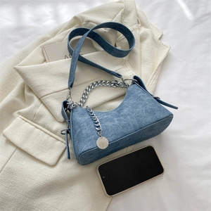 Close-up of denim crescent bag with chunky silver chain and round charm on white blazer