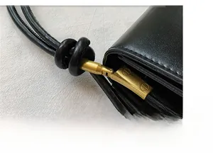 Detailed close-up of black leather bag strap with gold metal hardware and decorative knots
