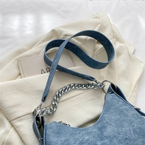 Close-up of blue denim crescent bag featuring silver chain link and textured fabric
