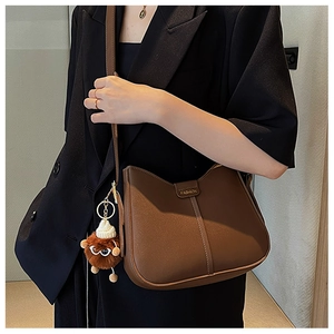 Detailed macro view of brown leather bag featuring FASHION embossing and a cute doll pendant