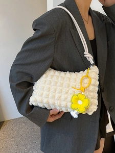 Minimalist beige puffy shoulder bag with floral charm worn over a dark grey blazer