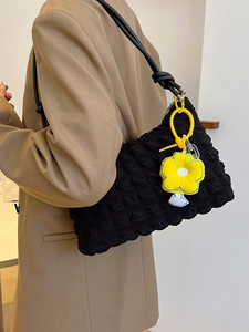 Minimalist black bubble quilted shoulder bag with a yellow sunflower plush charm on a model