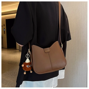 Detail of brown half-moon shoulder bag with vertical stitching and plush charm on model