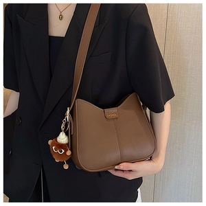 Detail view of a brown leather half-moon shoulder bag with a plush animal pendant