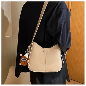 Close-up of minimalist khaki shoulder bag featuring fashion logo and plush monster charm