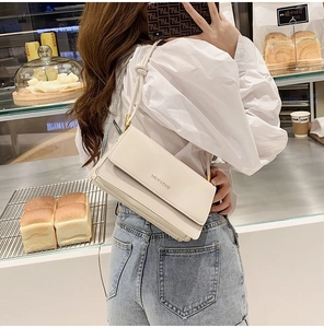 Detail of a creamy white rectangular baguette bag with a metal logo and slim strap