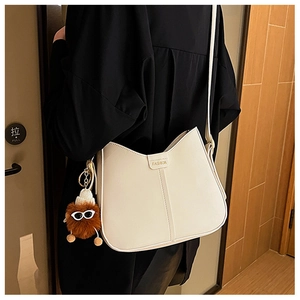 Close-up of minimalist cream hobo bag with fashion label and brown plush toy charm