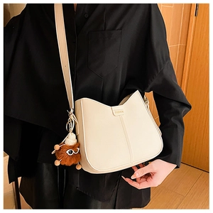 Detail of a creamy white saddle bag with FASHION logo and brown plush charm