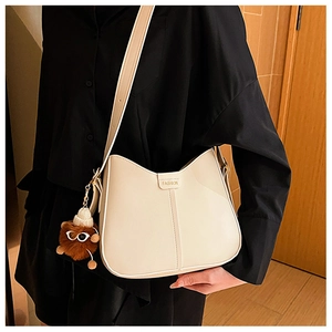 Detail of creamy white leather underarm bag with plush bear charm on black shirt