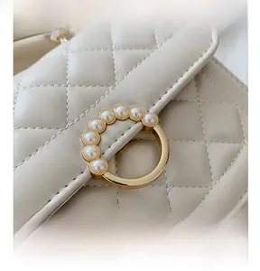 Close-up of cream quilted handbag featuring a golden ring handle with pearl embellishments