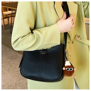 Close-up of black PU leather crescent bag with fashion tag and brown plush charm