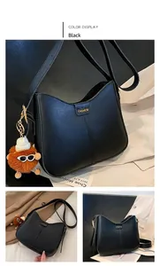 Detail view of black textured leather shoulder bag with orange charm and fashion lettering