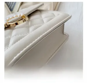 Macro shot of fine stitching details and pearl-embellished gold clasp on cream leather bag