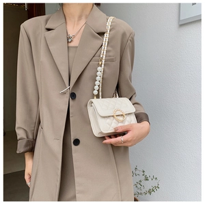 Detail of white quilted crossbody bag featuring gold pearl buckle and pearl chain strap