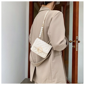 Detail of a beige quilted crossbody bag with pearl strap and elegant diamond lattice texture
