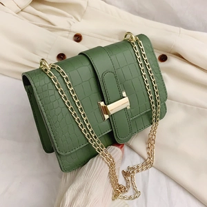 Sac carré vert foncé avec motif crocodile et bandoulière chaîne dorée sur tissu blanc