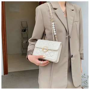 Detail view of cream quilted bag with pearl chain strap and gold clasp on model