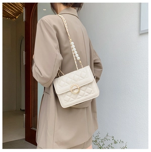 Detailed view of quilted chain bag with pearls worn over a camel blazer