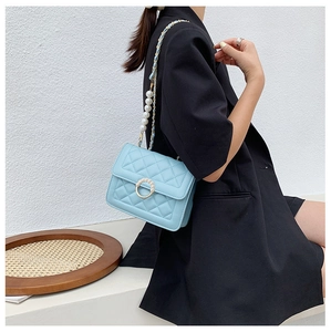 Detail of light blue quilted square bag with pearl buckle and decorative chain