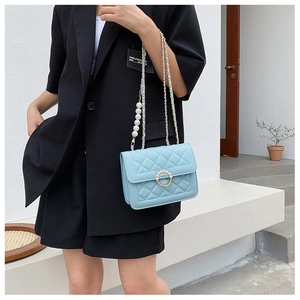 Detail of light blue quilted chain bag with pearl buckle shown on elegant model style