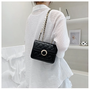 Detail of black quilted chain bag with pearls on elegant white blouse background