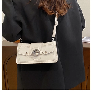 Détail d'un sac bandoulière blanc avec boucle métallique sur un blazer noir