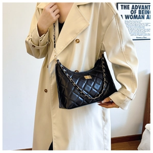 Chic black quilted crossbody bag with gold chain strap shown on a model in trench coat