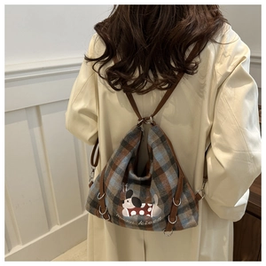Detail of plaid tote bag with cartoon puppy print and brown leather strap on trench coat