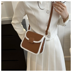 Detail of a brown leather crossbody bag with white faux fur trim and gold metal buckles