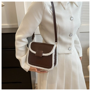 Detail of dark brown crossbody bag featuring white faux shearling trim and leather strap