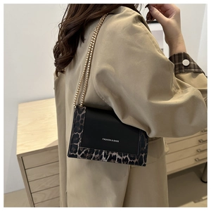 Detail of leopard print flap bag with gold chain strap on beige trench coat outfit
