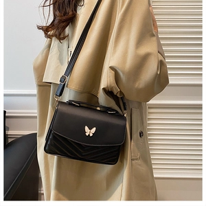 Detail of a black leather crossbody bag with golden butterfly clasp and V-shaped stitching