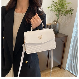 Close-up of white leather shoulder bag featuring a gold butterfly buckle and V-quilt pattern