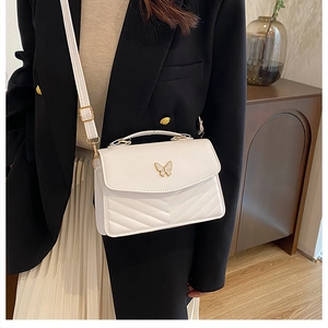 Chic white quilted shoulder bag with golden butterfly clasp shown on a model in a suit