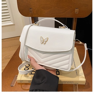 Detailed view of white quilted faux leather shoulder bag with golden butterfly emblem