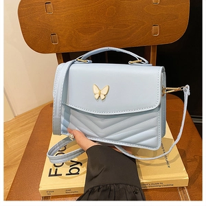 Close-up of light blue bag with V-shaped quilting and golden butterfly emblem