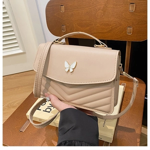 Close-up of beige chevron quilted bag with a delicate white butterfly metal buckle