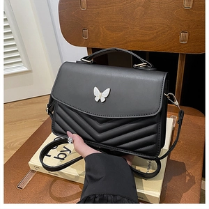 Detail of black crossbody bag with V-shaped quilting and white butterfly metal ornament