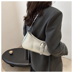 Detail view of a silver crescent underarm bag with metal buckle on a grey suit model