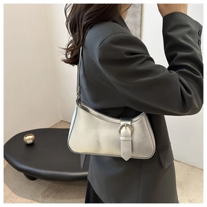 Side view of metallic silver crescent bag worn on shoulder by model in a minimalist room